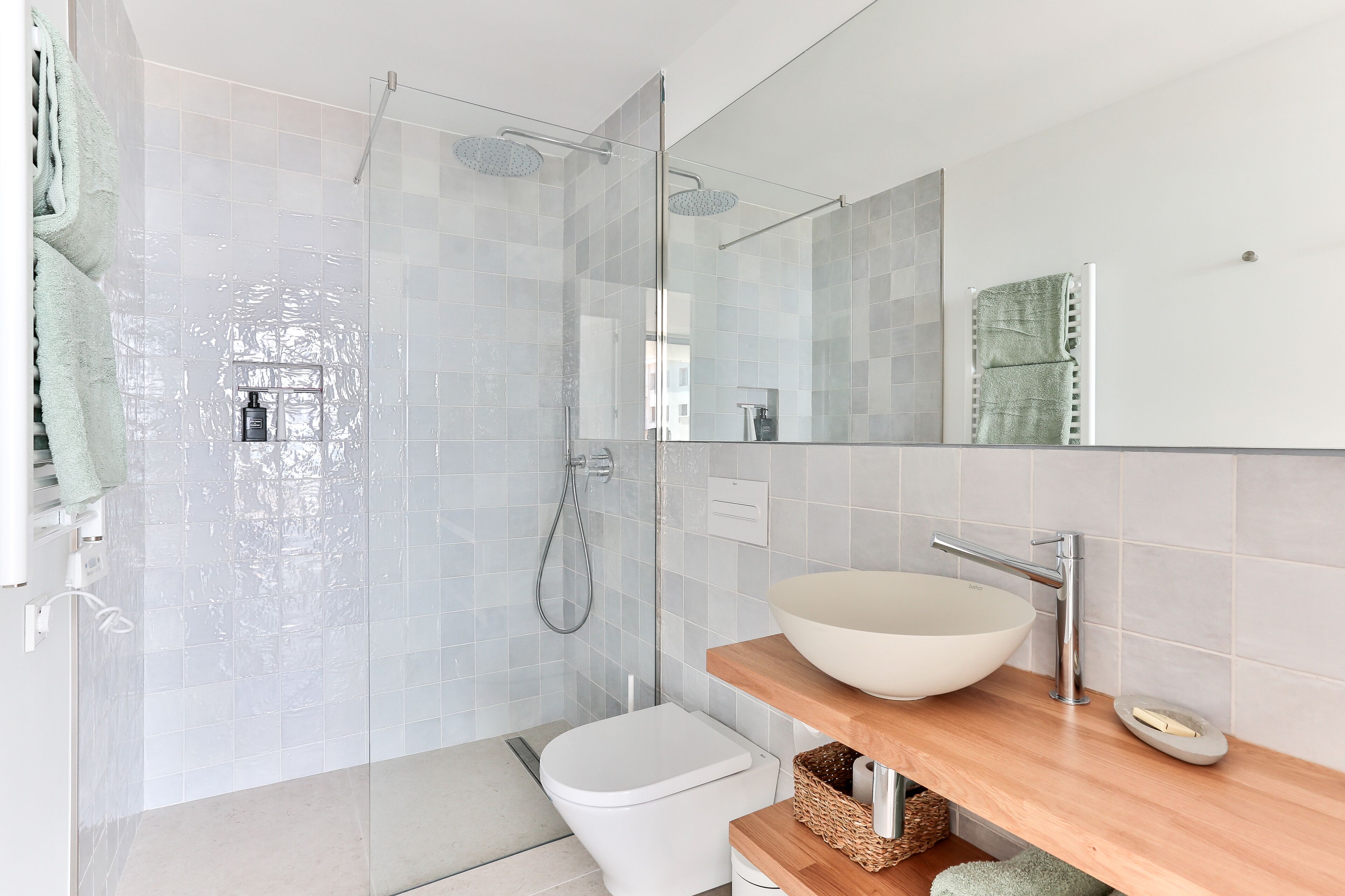 Een moderne badkamer met een douchecabine van glas, een wit toilet, een houten wastafelmeubel met een grote wasbak en een spiegel boven het meubel.