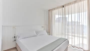 Una habitación de hotel con una cama grande, una mesita de noche, una lámpara y cortinas traslúcidas.