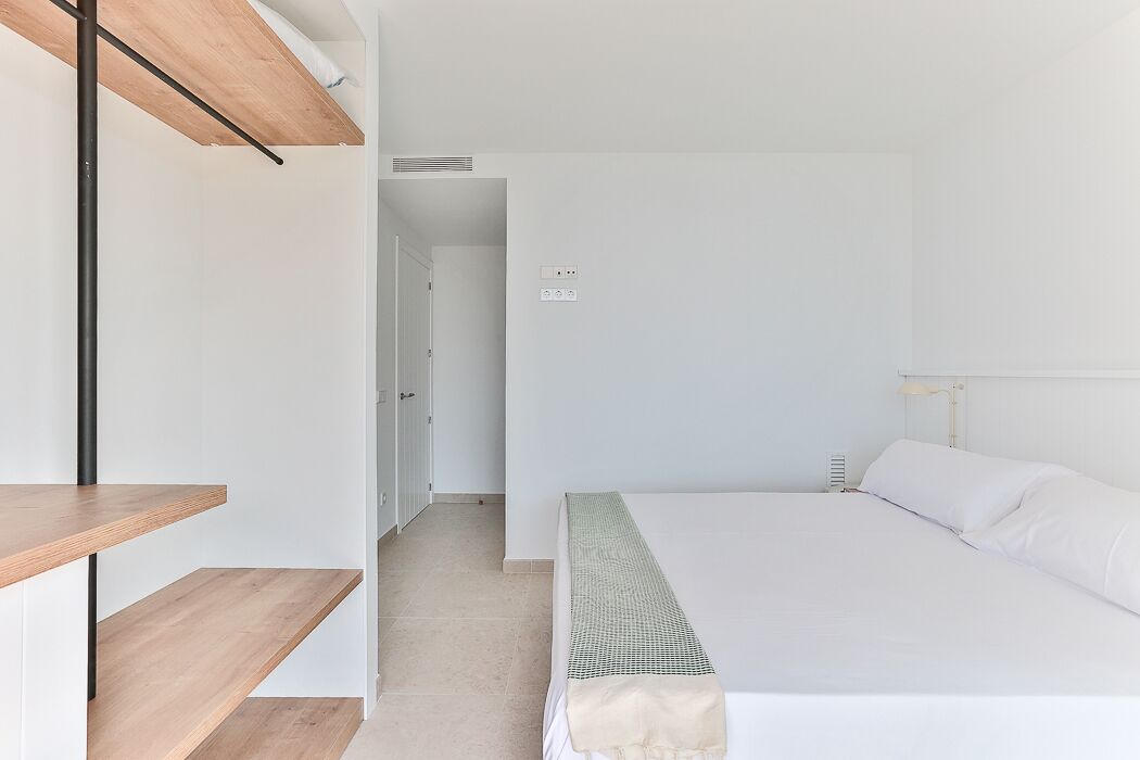 Een slaapkamer met een bed, een houten schapunit en een deur die naar een andere kamer leidt.