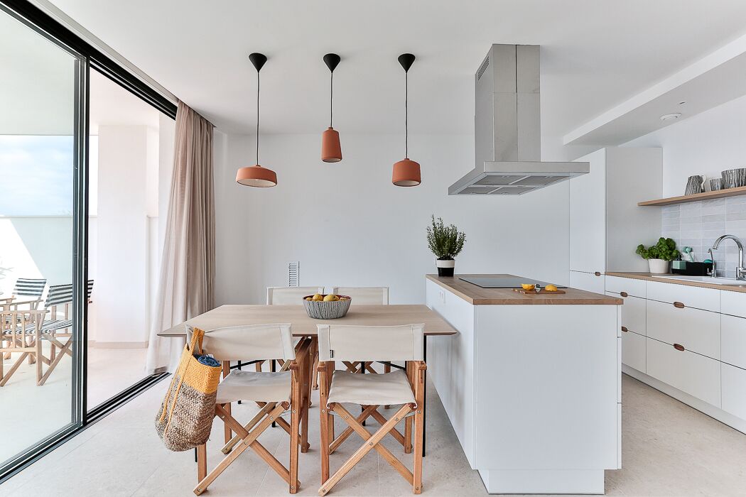 Una cucina moderna con mobili bianchi, un'isola in legno, luci a sospensione e un'ampia finestra.