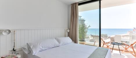 Habitación de hotel con cama, mesita de noche, lámpara y vista al mar.