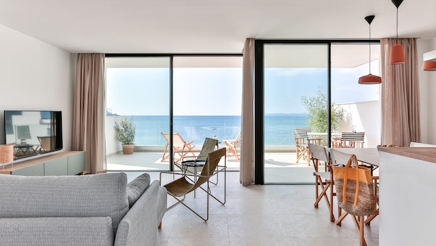 A modern living room with a large window, a sofa, and a dining area with chairs and a table. - ECO-APARTMENTS LA MARINEDA & HOTEL THALASSA SPORT & SPA (Roses)