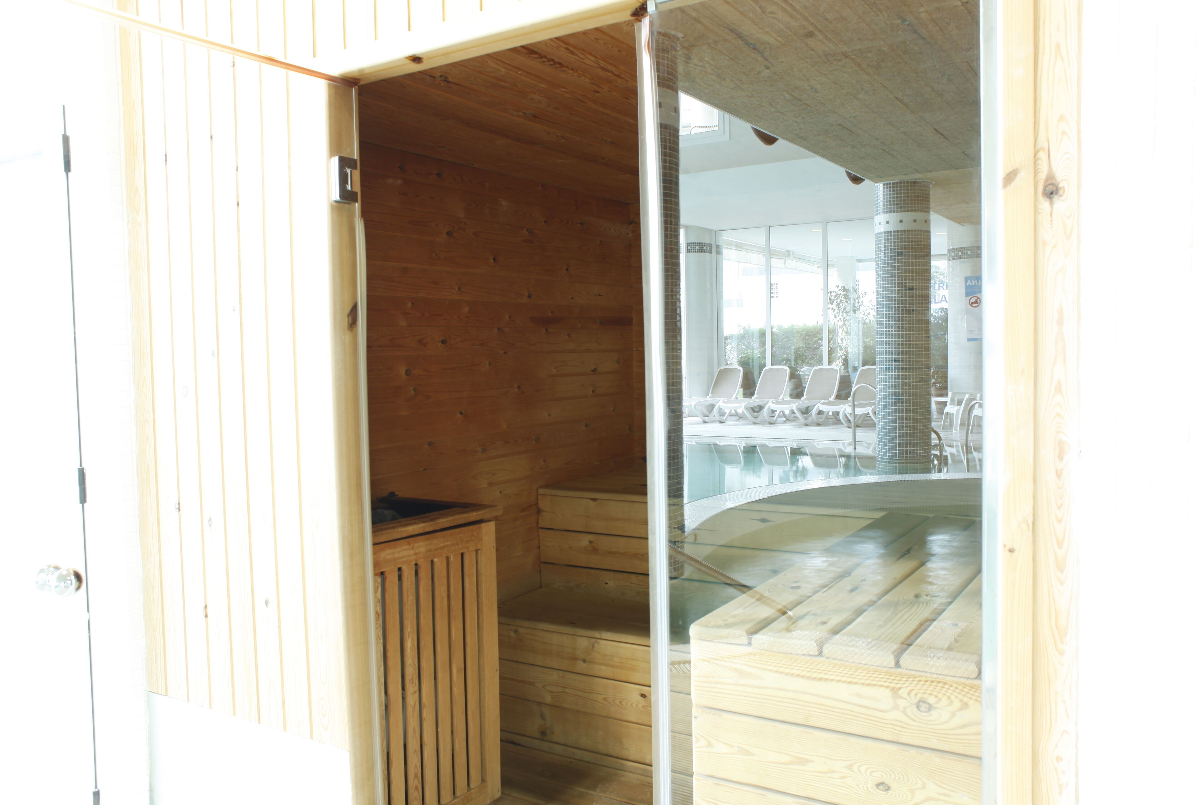 A wooden sauna with a glass door, wooden steps, and a bench.