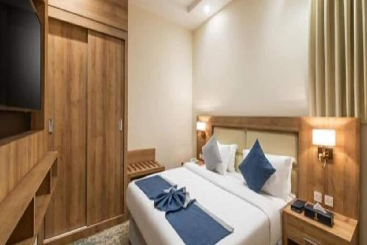 Una habitación de hotel con un armario de madera, una cama con ropa de cama azul y una mesita de noche con una lámpara.