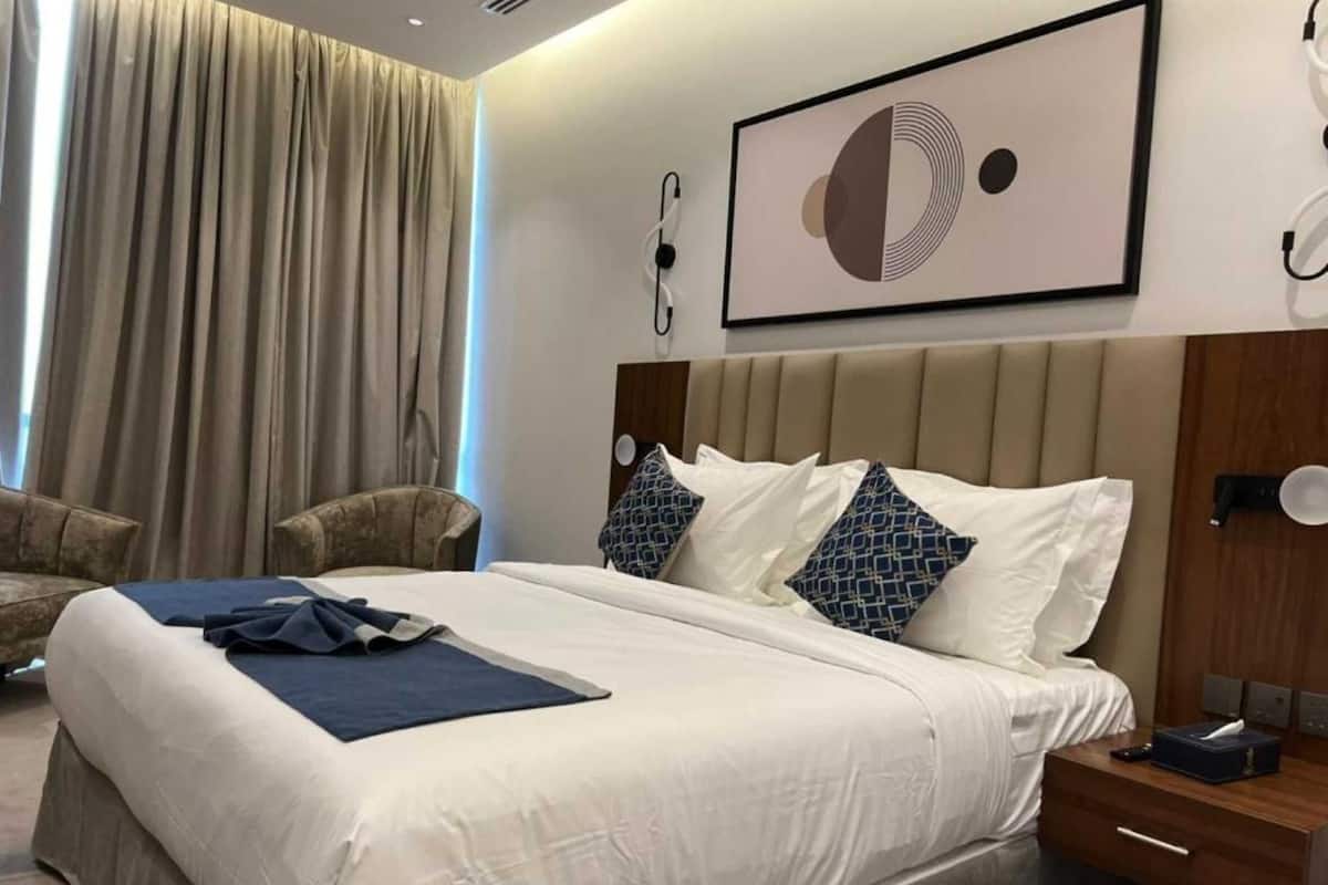 Habitación de hotel con una cama grande, cabecero, mesita de noche, una silla, un ventanal con cortinas y un teléfono en la pared.