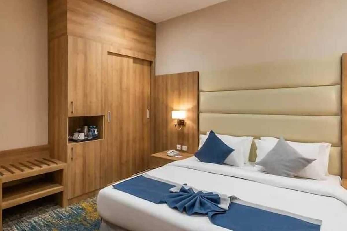 Una habitación de hotel con una cama, un armario de madera, una mesita de noche y una lámpara de pared.