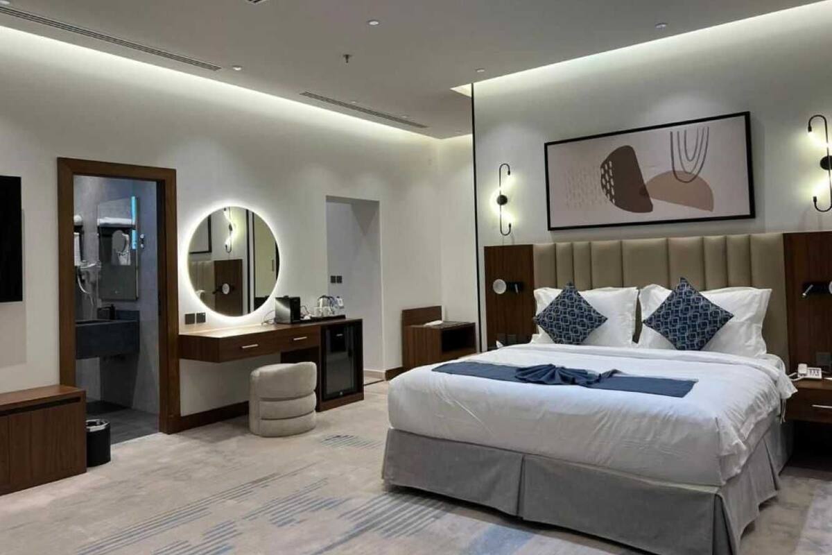 Una habitación de hotel moderna con una cama grande, un espejo redondo, una tocador y una mesita de noche.
