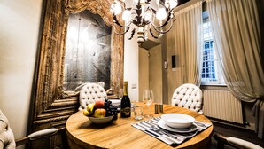 A dining area with a round wooden table, a chandelier, a large ornate mirror, and a window with curtains.