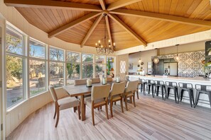 A spacious kitchen with a large island, wooden ceiling, and ample natural light from large windows.