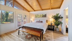 A bedroom with a wooden ceiling, a bed with white bedding, a bench, a nightstand with a lamp, and a potted plant. - Brand New 2 Bed/2.5 Bath Renovation, Centrally Located in Sedona (Sedona)