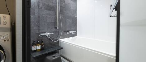 Une salle de bain moderne avec une grande baignoire, une douche équipée d’un pommeau flexible et un petit tabouret.