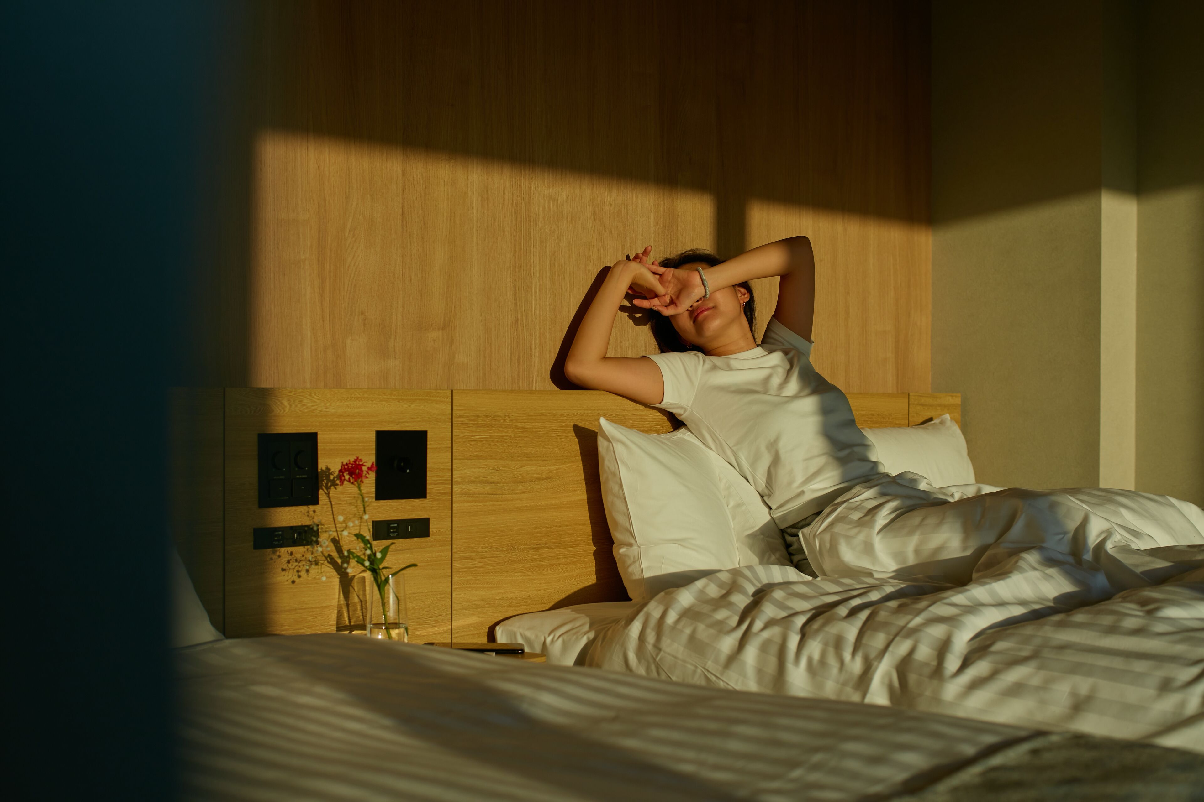 A bed with white bedding, a wooden headboard, and a nightstand with a vase of flowers.