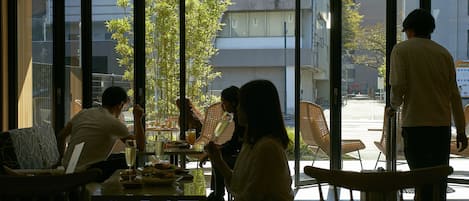 An indoor dining area with large windows, a table with food and drinks, and several people seated.