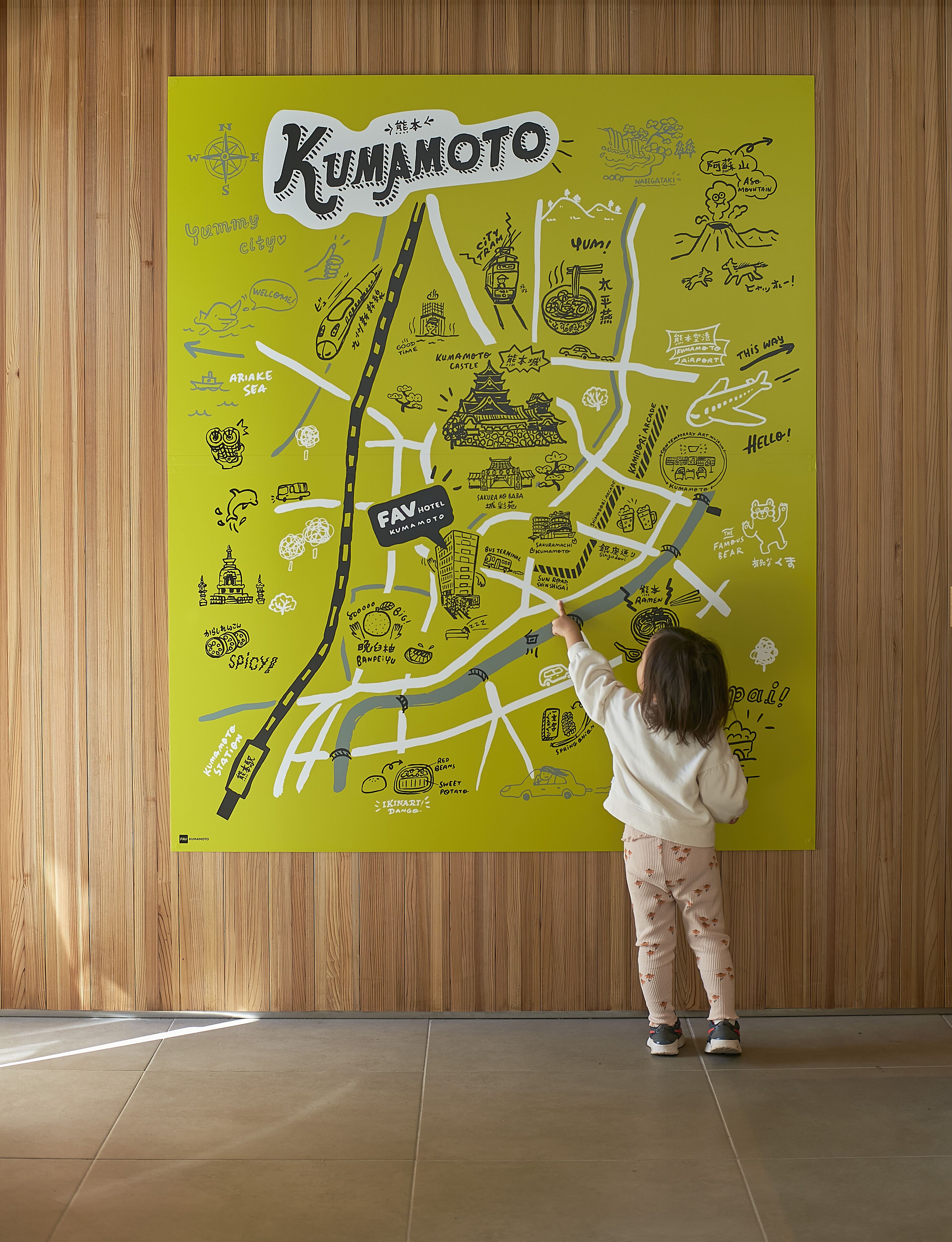 Un enfant désigne du doigt une carte colorée de la ville de Kumamoto, mettant en évidence les principaux monuments et les sites touristiques.