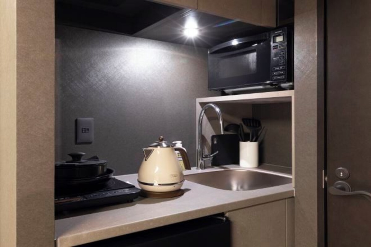A compact kitchen with a microwave, kettle, and sink.