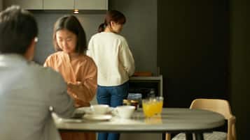 Un comedor con una mesa preparada para dos personas, una persona de pie junto a la encimera y una silla con cojín.
