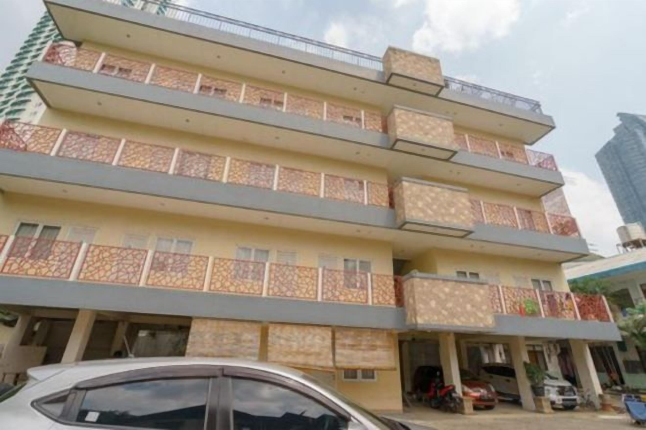 A multi-story building with balconies, a car parked in front, and a clear sky.
