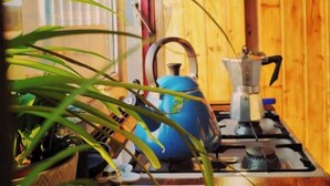 A kitchen with a blue kettle, a stove, and a hanging pot.