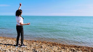 A person standing on a pebbled beach, facing the sea.
