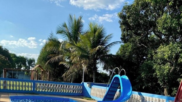 Une piscine avec un toboggan bleu, entourée d’une terrasse carrelée et de palmiers.