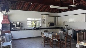 Une cuisine spacieuse avec des meubles blancs, une table à manger avec des chaises, un ventilateur et un four en briques.