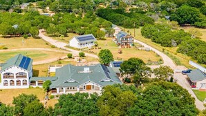 A residential area with multiple houses, including a large house with solar panels and a smaller house with a garage. - Cabin B (Casa Blanca), 1BR/1BA, Sleeps 4, Porch, Grill (Kerr County)
