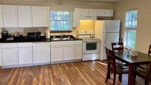 A compact kitchen with white cabinets, a stove, a refrigerator, and a dining table with chairs. - Cabin B (Casa Blanca), 1BR/1BA, Sleeps 4, Porch, Grill (Kerr County)