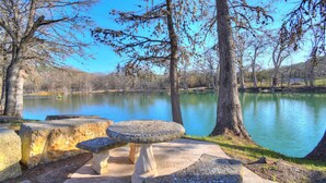 A serene lakeside setting with a stone bench and table, surrounded by trees and a clear sky. - Cabin B (Casa Blanca), 1BR/1BA, Sleeps 4, Porch, Grill (Kerr County)