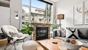 Una sala de estar moderna con chimenea, un ventanal grande, un sofá, un sillón y una mesa de centro.