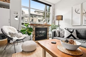 A modern living room with a fireplace, a large window, a sofa, a chair, and a coffee table.