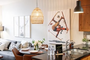 Et moderne køkken med spiseplads, med et stort maleri, en fletvævslampe og en velkomstplakat.