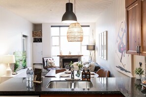 A modern kitchen with a central island, a hanging light fixture, and a dining area with a sofa and table.