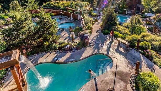 Un complejo turístico con varias piscinas rodeado de exuberante vegetación y montañas al fondo.