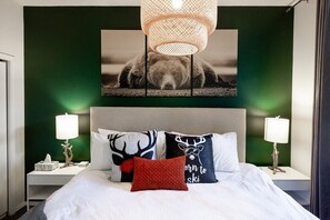 Une chambre à coucher avec un lit, deux tables de chevet, une lampe fixée au mur et un tableau encadré au-dessus du lit.