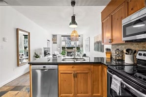 A modern kitchen with wooden cabinets, a stainless steel dishwasher, and a black countertop.