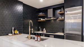 A modern kitchen with a marble countertop, a stainless steel refrigerator, and a black hexagonal backsplash.