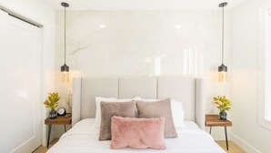 A bedroom with a large bed, two bedside tables with lamps, a marble headboard, and a view of the outside.
