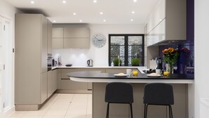 A modern kitchen with a central island, two bar stools, a clock, and a window with a view. - SUPERB 3 BEDROOM AND OFFICE COVENT GARDEN HOUSE (London)