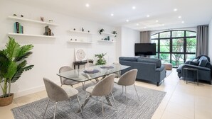 A modern living room with a glass dining table, grey sofas, and a large window with a view of greenery. - SUPERB 3 BEDROOM AND OFFICE COVENT GARDEN HOUSE (London)