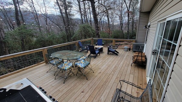 A wooden deck with a table and chairs, surrounded by a metal railing, overlooking a forested area. - Gooseberry House - Full 3 bedroom, 2.5 bath house rental across the road from Campground. Inculdes access to communal areas of campground including Nantahala River and self-guided farm tour. (Franklin)