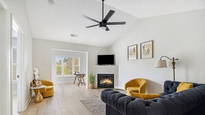 Una sala de estar moderna con chimenea, ventilador de techo y televisor montado en la pared.