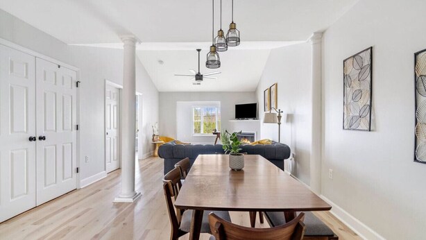 Un comedor amplio con una mesa y sillas de madera, un sofá gris al fondo y lámparas colgantes arriba.