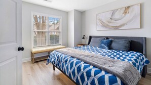 Un dormitorio con una cama grande, un banco junto a la ventana y una lámpara en el techo.