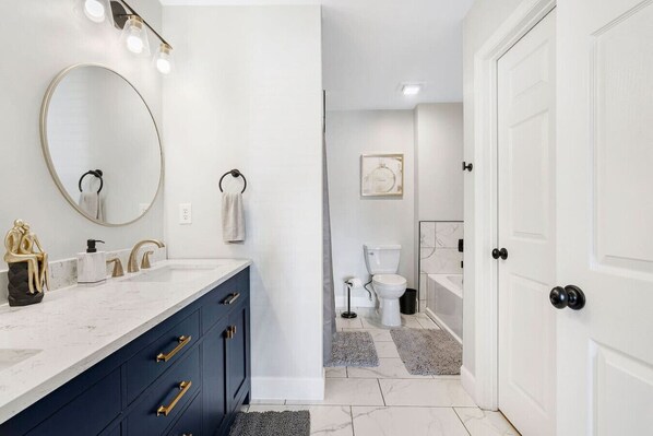 A modern bathroom with a marble sink, dark blue cabinets, and a large mirror.