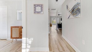 Un pasillo amplio con piso de madera, una cita enmarcada en la pared y un mueble de ratán.