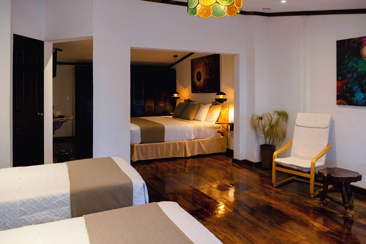 Quarto de hotel com duas camas, uma cadeira, um vaso de plantas e um quadro na parede.