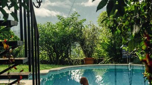 A swimming pool with a person lying on the edge, surrounded by greenery and a metal fence. - Hotel Juayua (Juayua)