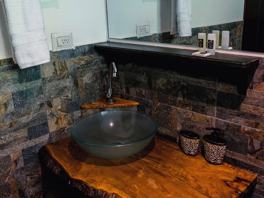 A modern bathroom with a large glass bowl sink, wooden vanity, and stone walls.