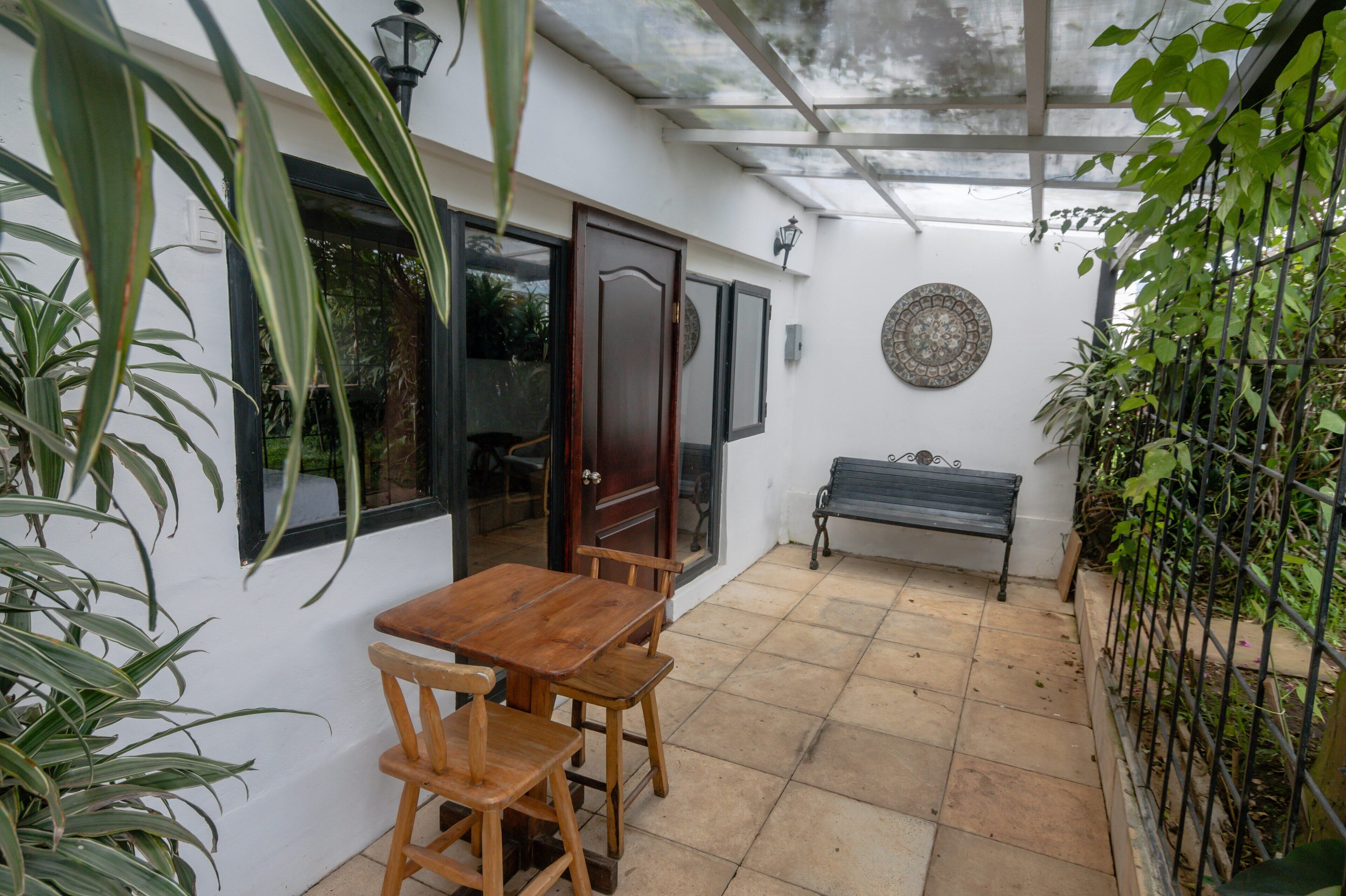 A covered patio with a wooden table and chairs, a bench, and a decorative wall plate.