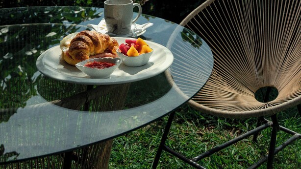 A table with a croissant, fruit, and a cup, set outdoors with a chair and a mountain view in the background. - Hotel Juayua (Juayua)
